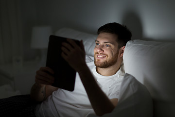 Image showing young man with tablet pc in bed at home bedroom