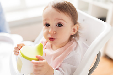 Image showing baby drinking from spout cup in highchair at home