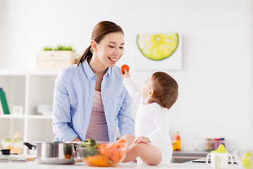 Image showing baby feeding mother with carrot at home kitchen