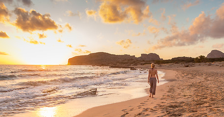 Image showing Woman walking on sandy beach at sunset.