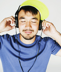 Image showing young asian man in hat and headphones listening music on white b