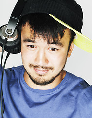 Image showing young asian man in hat and headphones listening music on white b