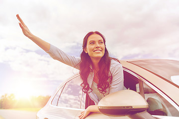 Image showing happy young woman driving in car and waving hand