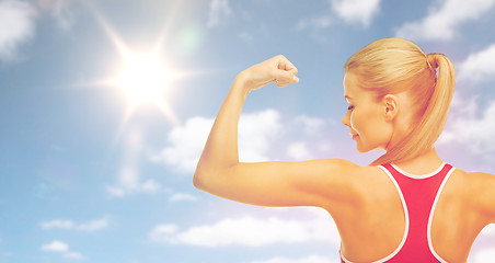 Image showing happy sporty woman showing biceps over sky and sun