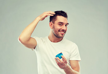 Image showing happy young man styling his hair with wax or gel