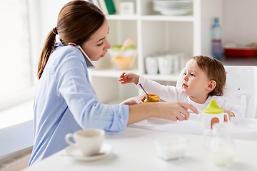 Image showing mother with smartphone feeding baby at home