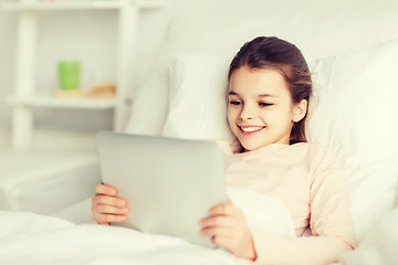 Image showing happy girl lying in bed with tablet pc at home