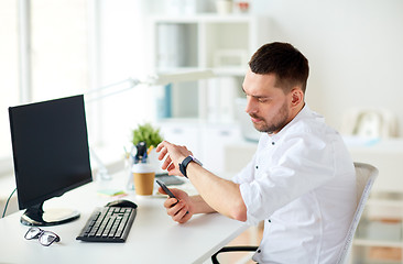 Image showing businessman with smartphone and computer at office