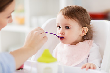 Image showing happy mother feeding baby with puree at home