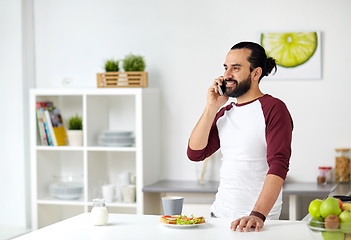 Image showing man calling on smartphone and eating at home