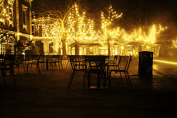 Image showing empty night restaurant, lot of tables and chairs with noone, magic fairy lights on trees like christmas celebration