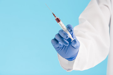 Image showing Hand in a blue glove holding syringe on blue