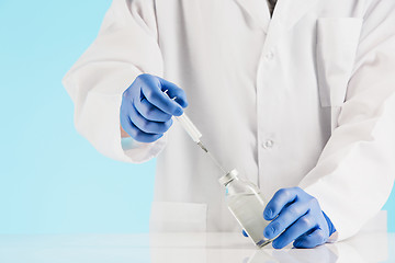 Image showing Hand in a blue glove holding syringe on blue