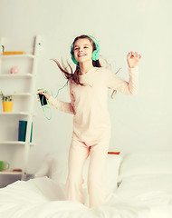 Image showing girl jumping on bed with smartphone and headphones