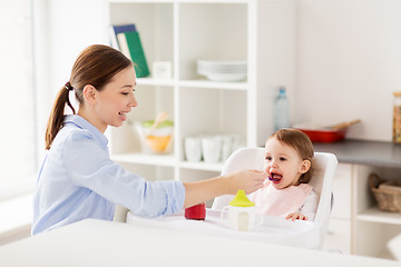 Image showing happy mother feeding baby with puree at home