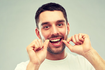 Image showing man with dental floss cleaning teeth over gray