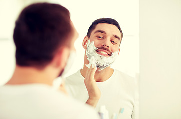 Image showing happy man applying shaving foam at bathroom mirror