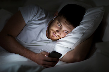 Image showing man with smartphone and earphones in bed at night