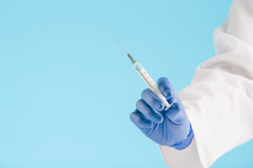 Image showing Hand in a blue glove holding syringe on blue