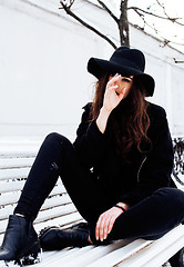 Image showing young pretty modern hipster girl waiting on bench at winter snow park alone, lifestyle people concept 