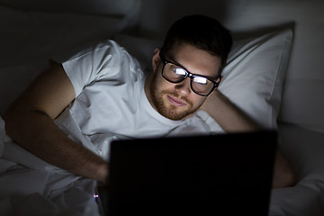 Image showing young man with laptop in bed at home bedroom