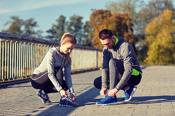 Image showing smiling couple tying shoelaces outdoors