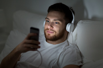 Image showing man with smartphone and headphones in bed at night