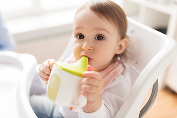 Image showing baby drinking from spout cup in highchair at home