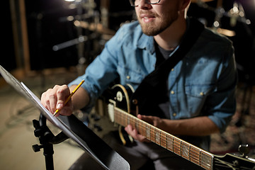 Image showing man with guitar writing to music book at studio