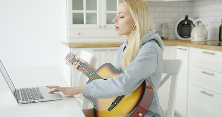 Image showing Woman using laptop while playing guitar