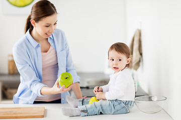 Image showing mother giving green apple to baby at home kitchen