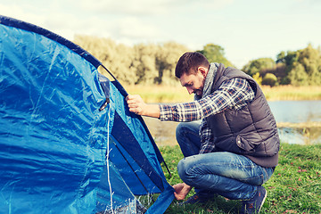 Image showing happy man setting up tent outdoors