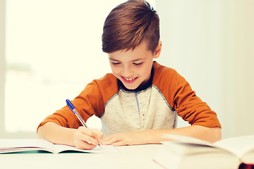 Image showing smiling student boy writing to notebook at home