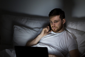 Image showing man with laptop calling on smartphone at night