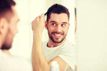 Image showing happy man brushing hair  with comb at bathroom