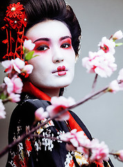 Image showing young pretty geisha in black kimono among sakura, asian ethno close up concept