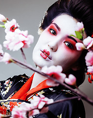 Image showing young pretty geisha in black kimono among sakura, asian ethno close up