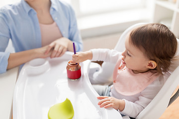 Image showing baby girl with spoon eating puree from jar at home