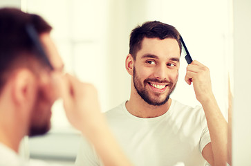 Image showing happy man brushing hair  with comb at bathroom