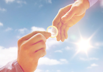 Image showing close up of male gay couple hands giving condom