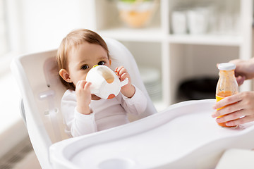 Image showing baby drinking from spout cup in highchair at home