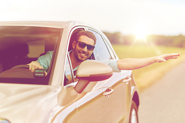 Image showing happy man in shades driving car and waving hand