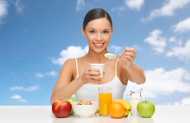 Image showing happy woman with fruits, cereals eating yogurt