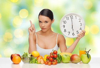 Image showing woman with food and big clock sitting at table