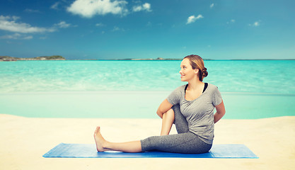 Image showing woman making yoga in twist pose on mat over beach 