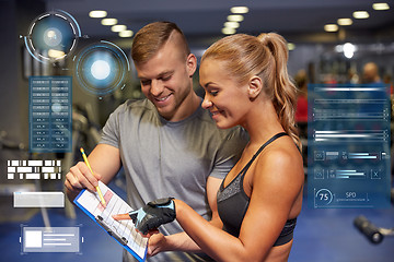 Image showing smiling woman with trainer and clipboard in gym