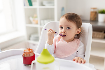 Image showing baby girl with spoon eating puree from jar at home