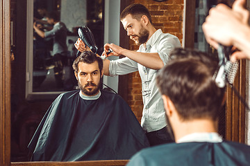 Image showing Young handsome barber making haircut of attractive man in barbershop