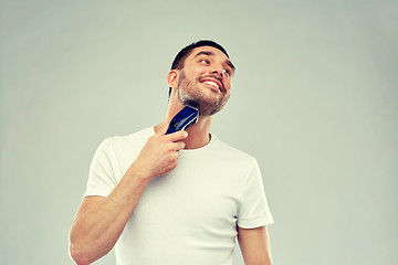 Image showing smiling man shaving beard with trimmer over gray