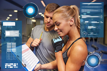 Image showing smiling woman with trainer and clipboard in gym